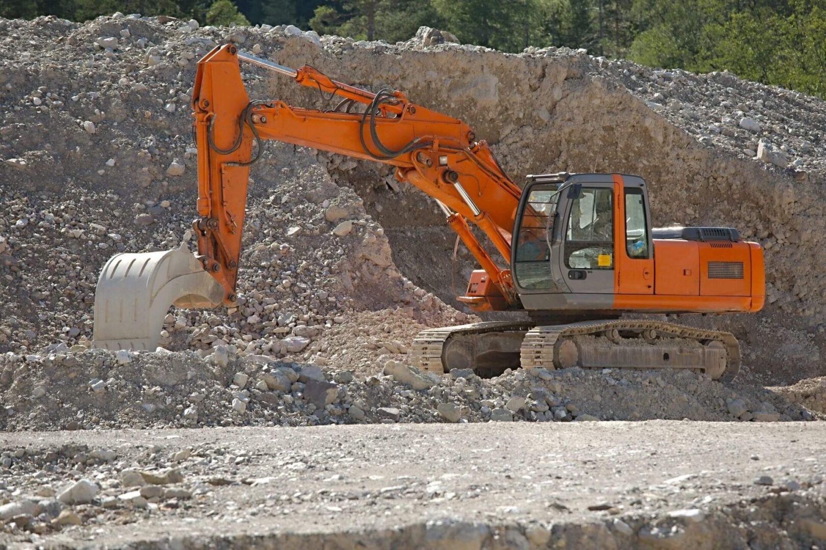 Orange excavator digging at a rocky site.