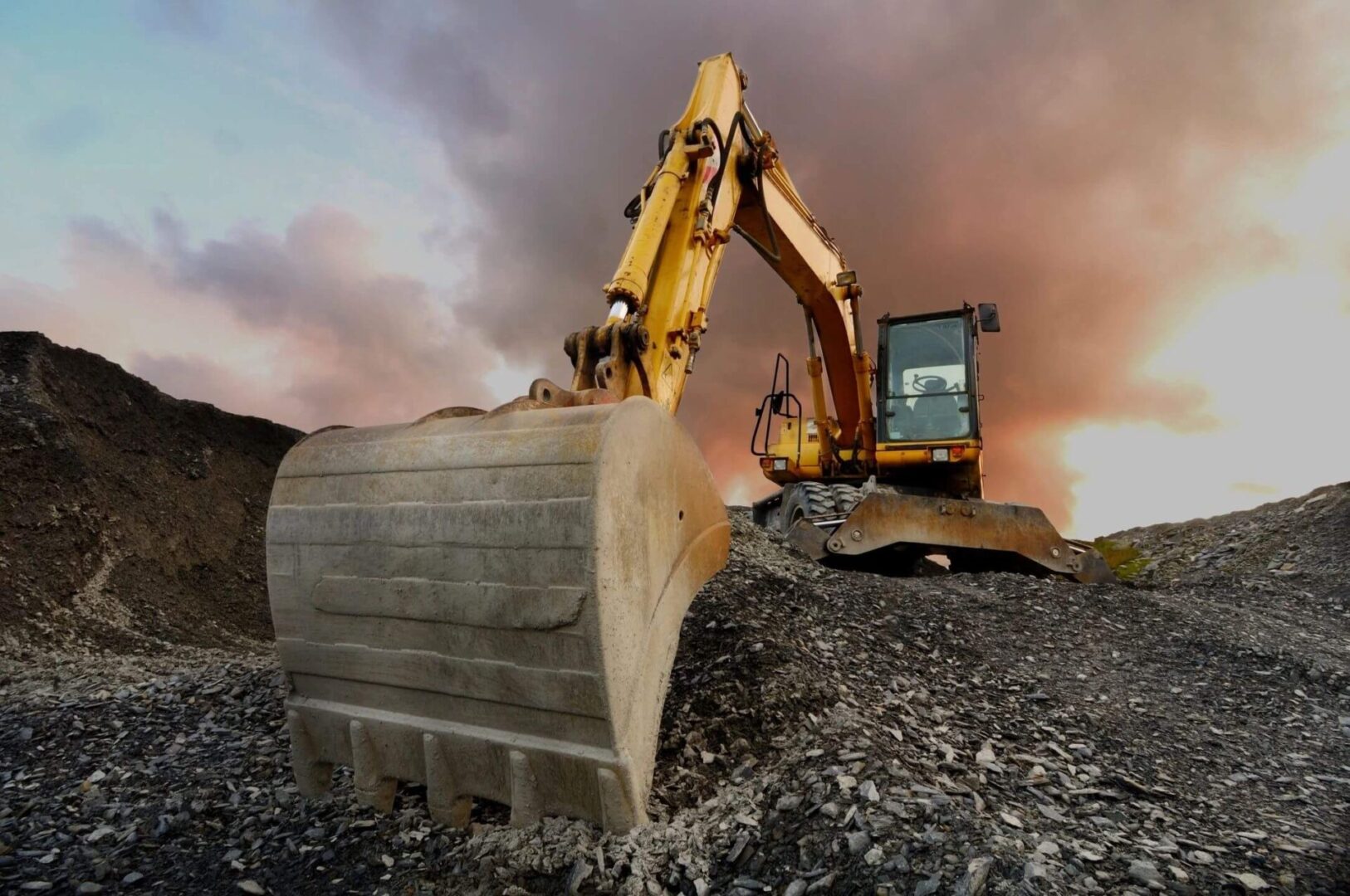 Excavator on rocky terrain at sunset.