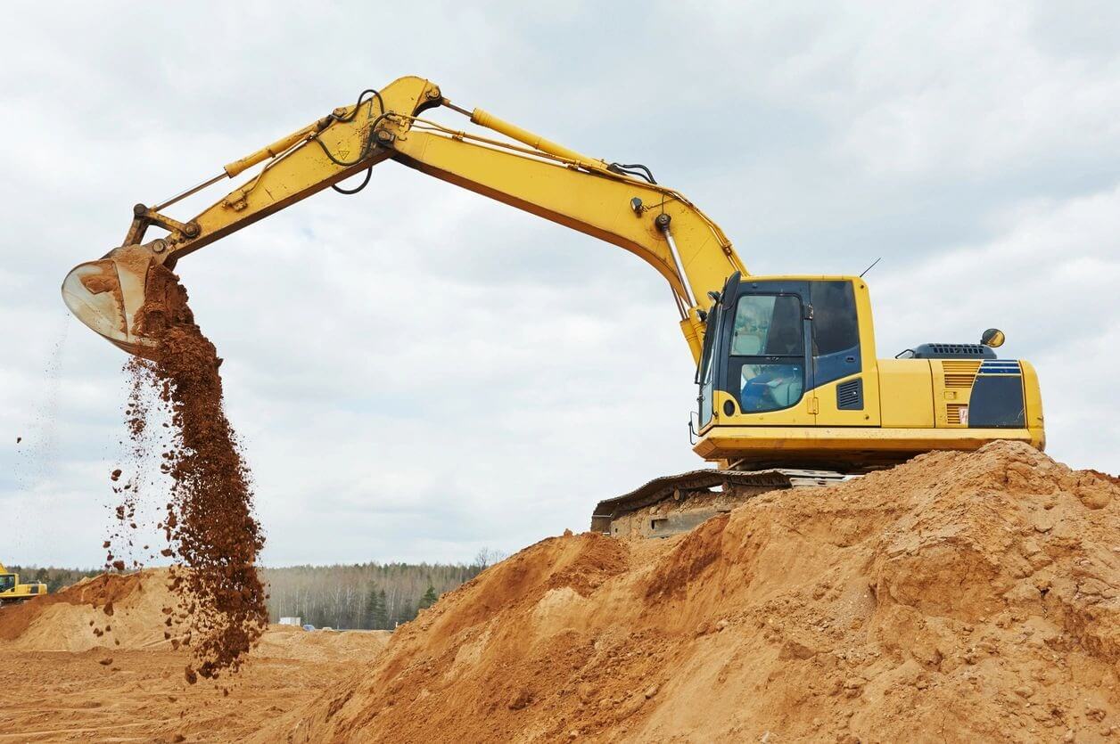 Yellow excavator pouring dirt on mound.