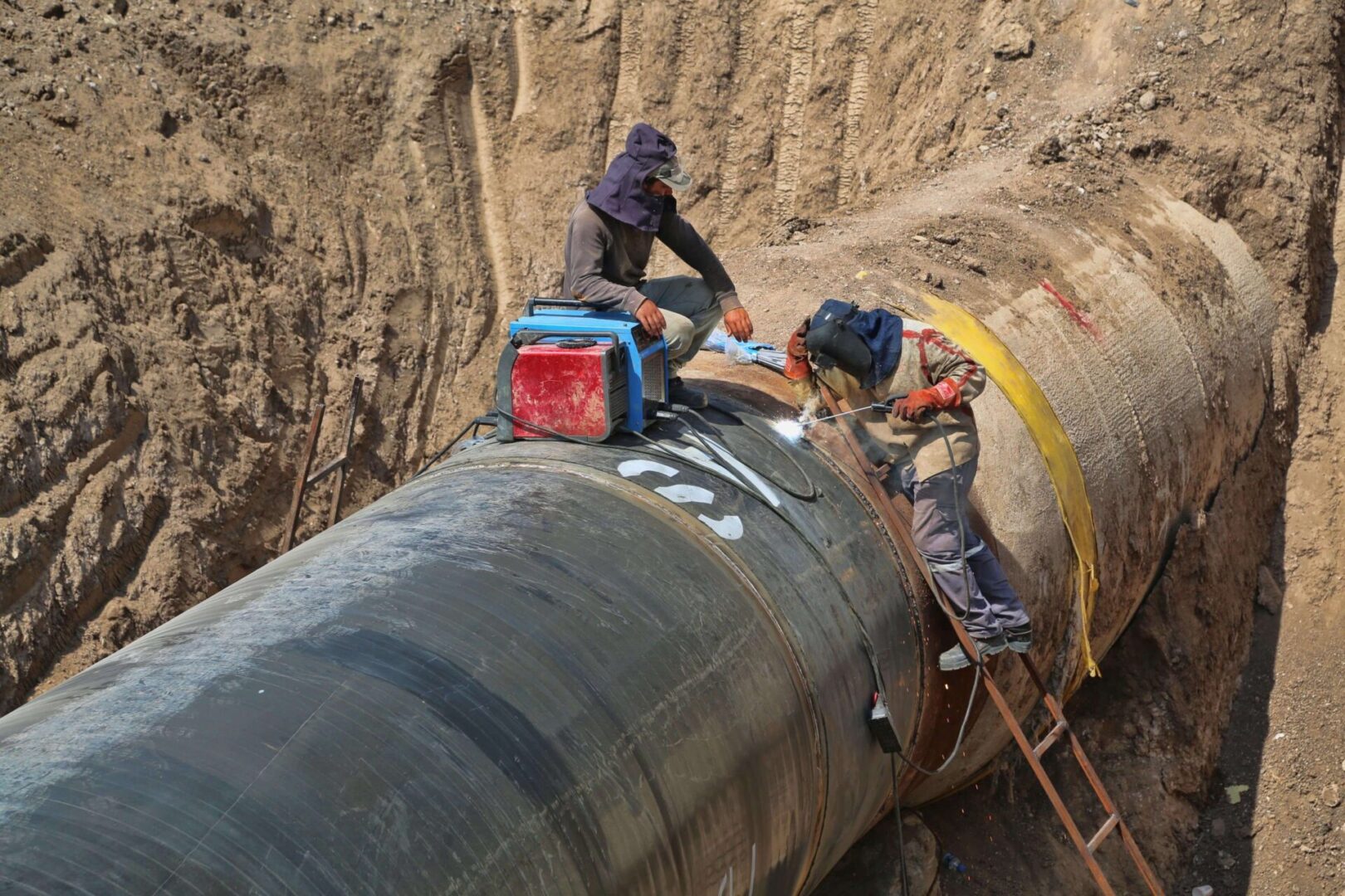 Workers welding large underground pipeline.